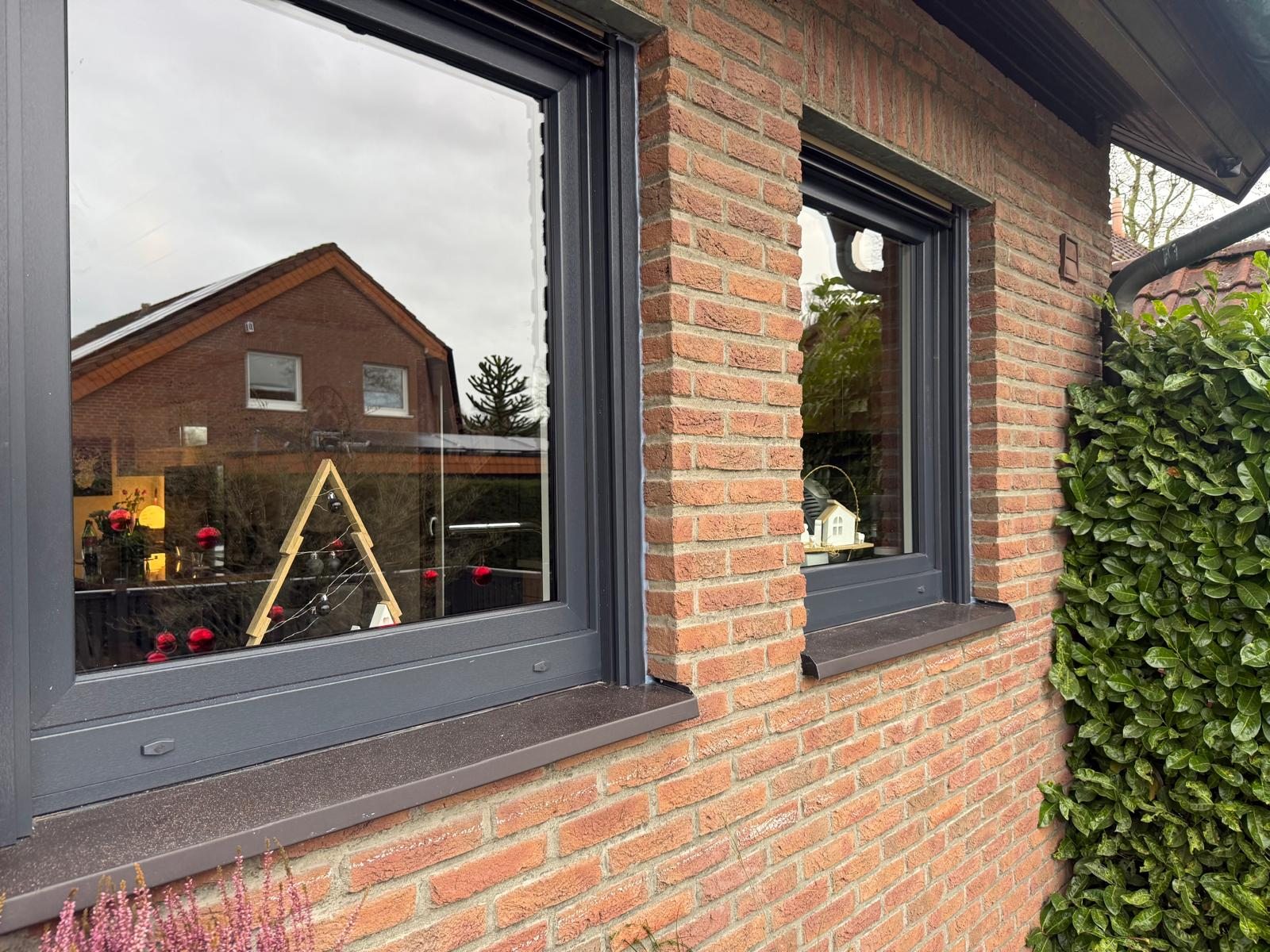 Zwei anthrazitfarbene Fenster in einer roten Klinkerfassade, im Glas spiegelt sich das Nachbarhaus