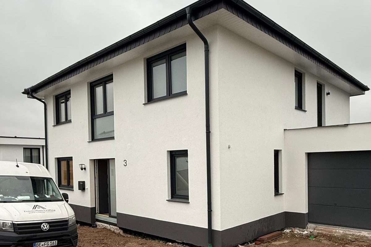 Weißer Neubau mit anthrazitfarbenen Fenstern und farblich passendem Garagentor, links der Firmenwagen