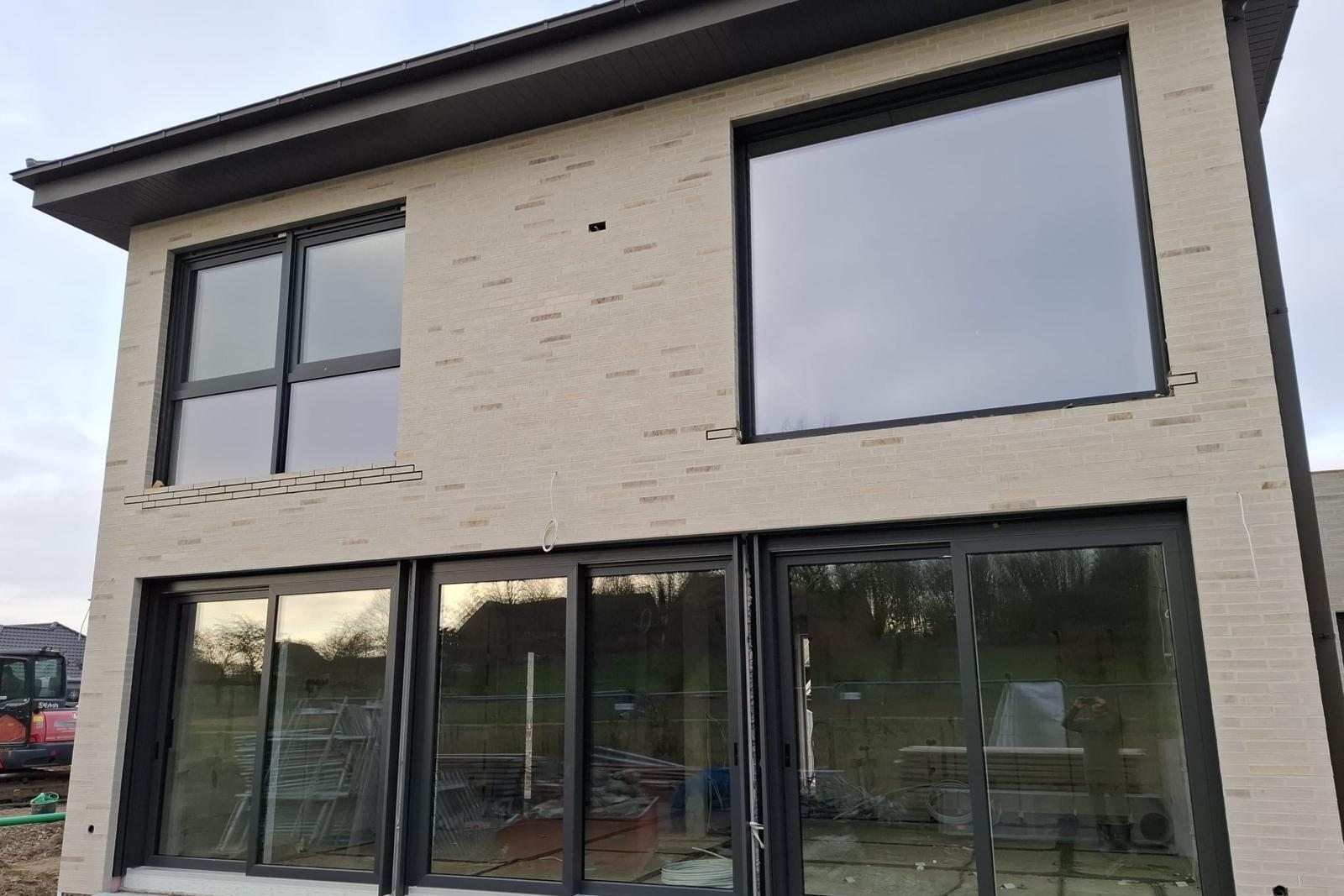 Zweigeschossiger Neubau mit heller Klinkerfassade, bodentiefen Fenstertüren im Erdgeschoss und großen dunklen Fenstern im Obergeschoss